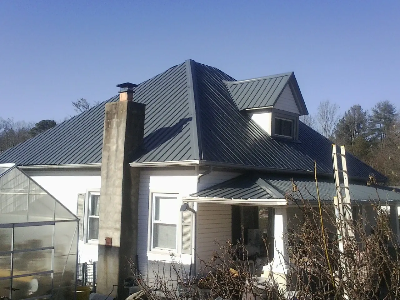 Dark blue standing seam metal roof on a white farmhouse with dormer — Slate & Tile Roof Repair by Roofing Brothers in Shady Valley