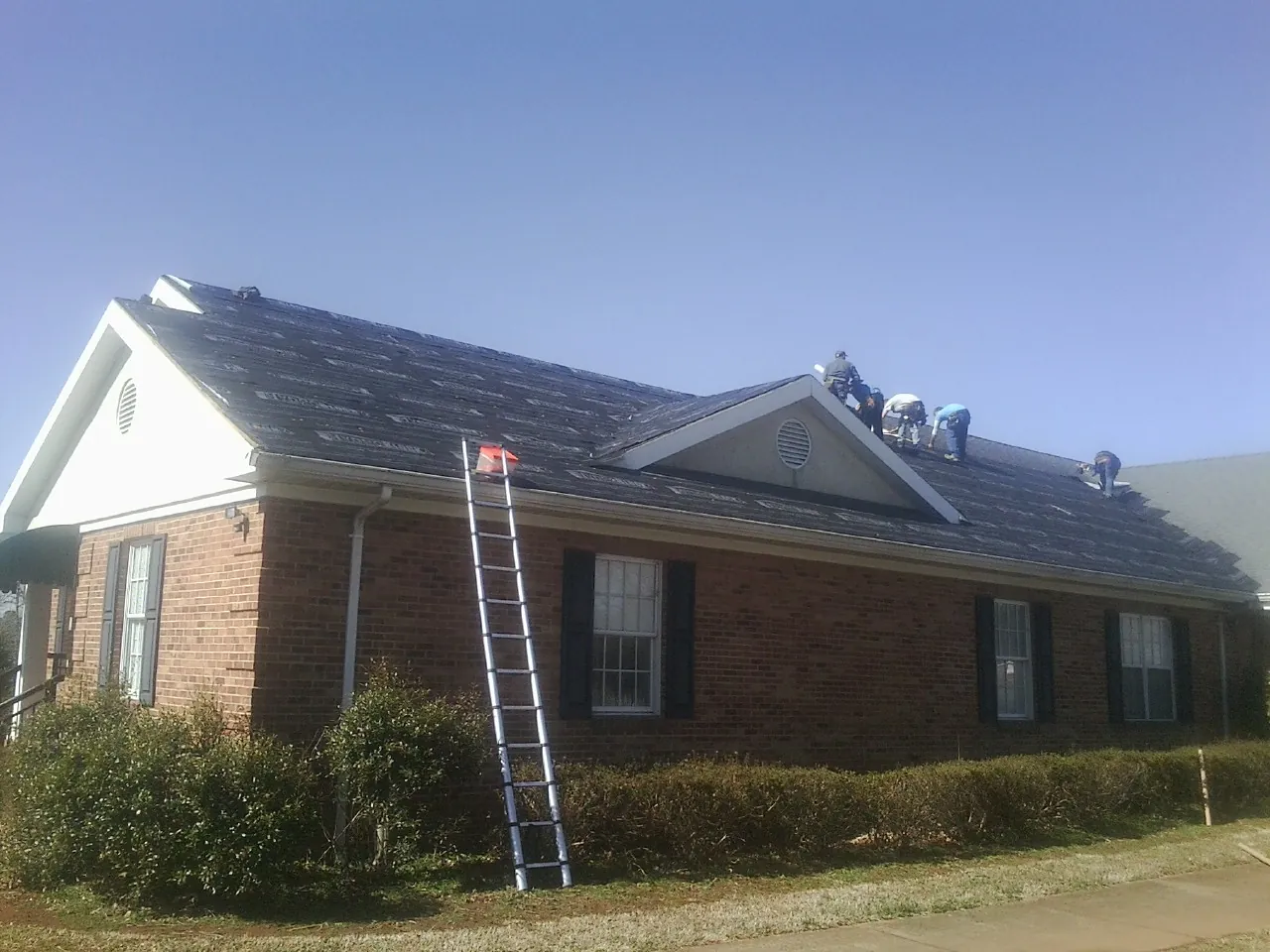 Crew tearing shingles off a brick ranch roof with a ladder set — Emergency Roof Repair work by our crew in Shady Valley