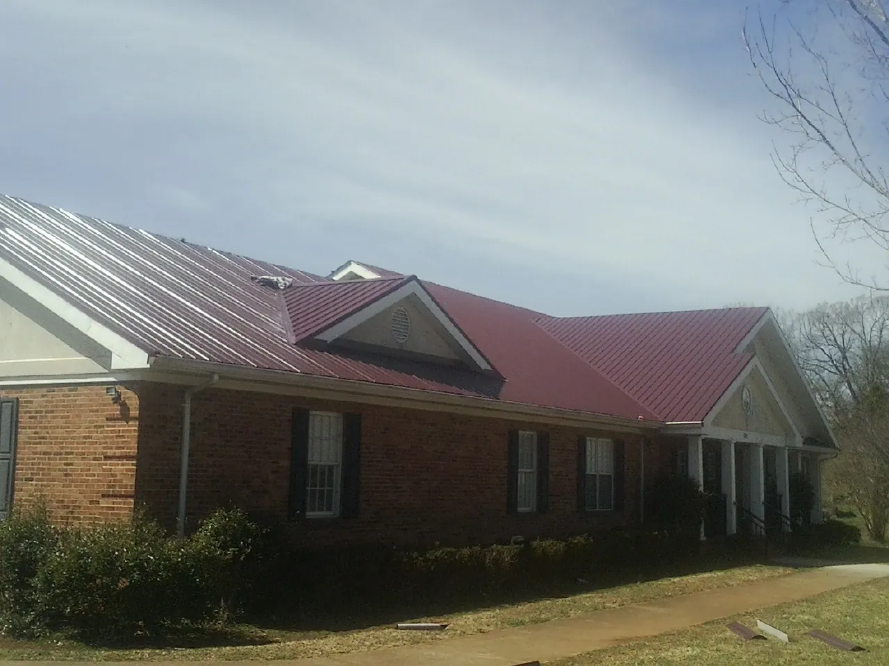 Red metal roof with gabled entries on a long brick building, from a Hail Damage Roof Repair job in Shady Valley