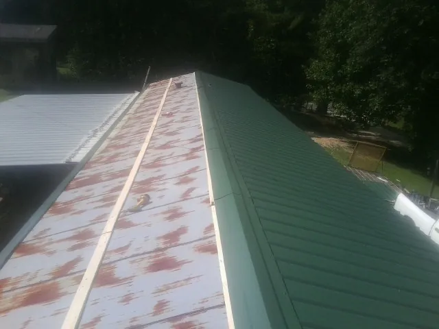 Old rusted panels beside newly installed green metal roofing — Wind Damage Roof Repair by Roofing Brothers in Shady Valley