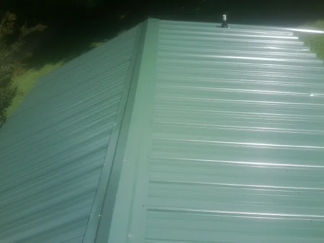 New green metal panels meeting at the ridge of a roof — Flat Roof Repair work by our crew in Shady Valley