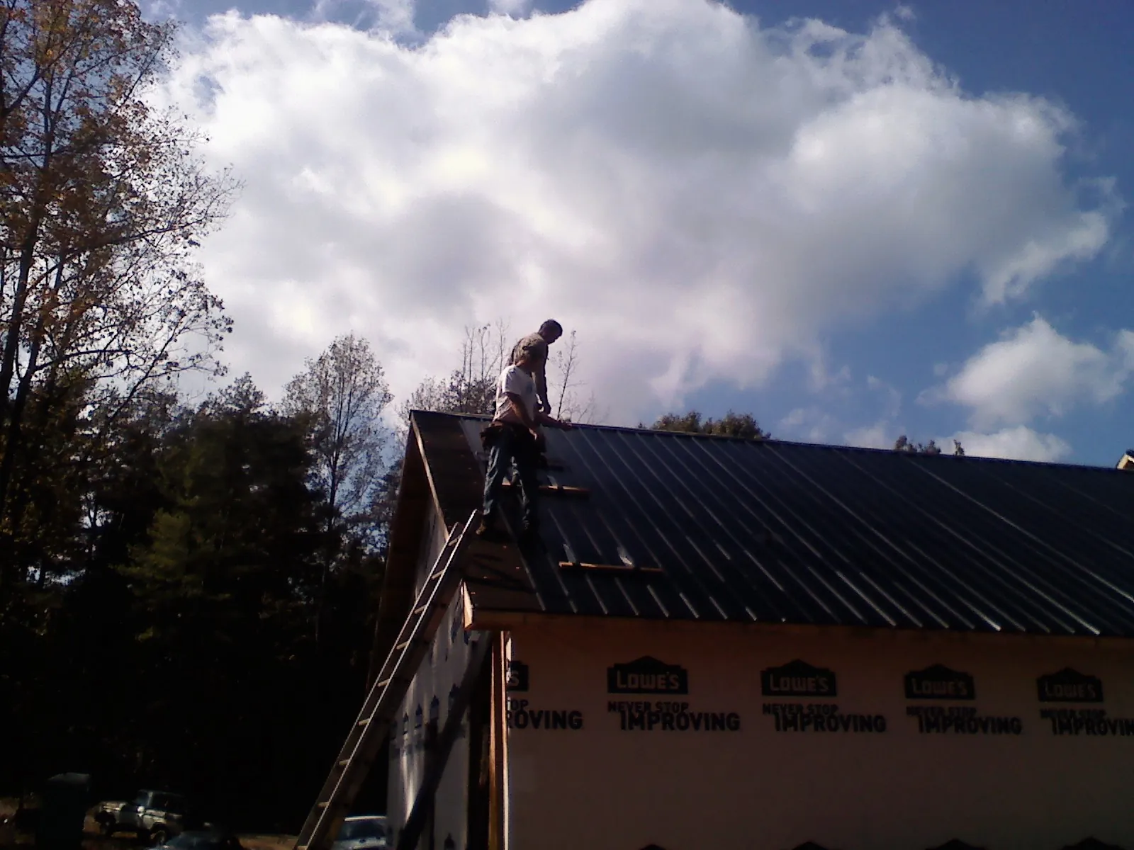 Roofer fastening dark metal panels high against a cloudy sky, from a Roof Inspection job in Shady Valley