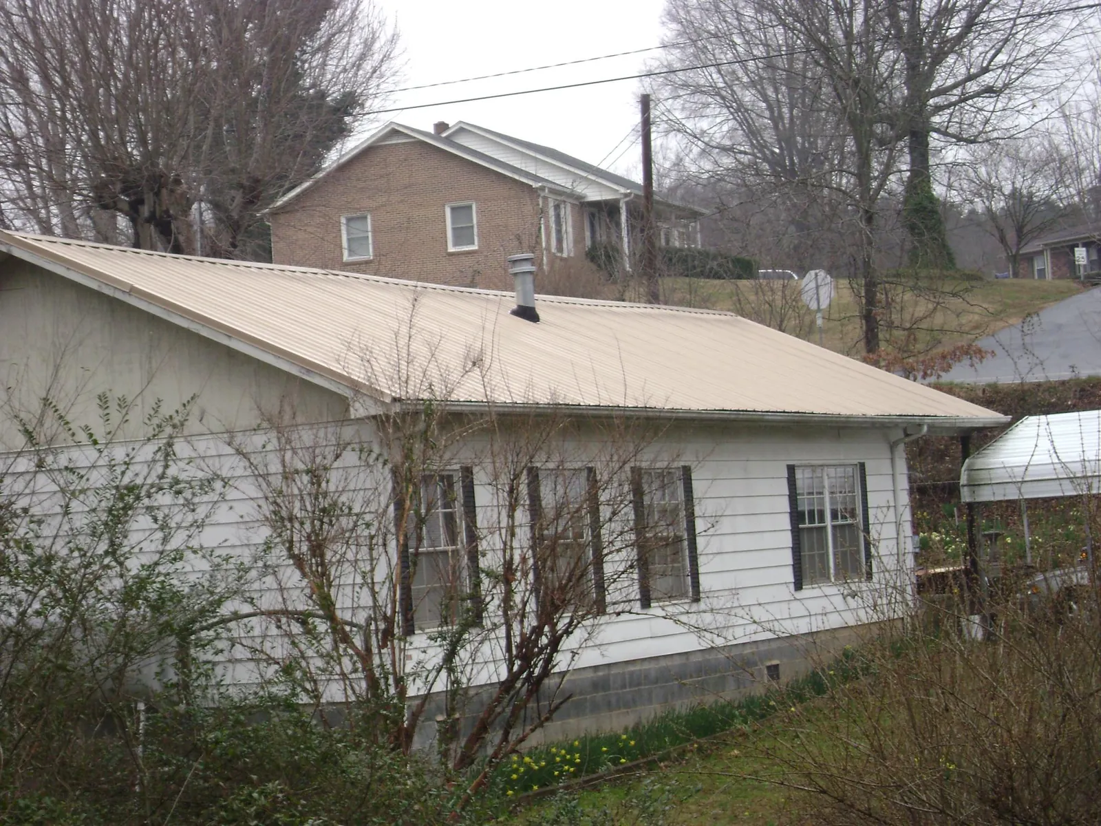 Tan metal roof on a white sided house set into a hillside — Commercial Roofing by Roofing Brothers in Shady Valley